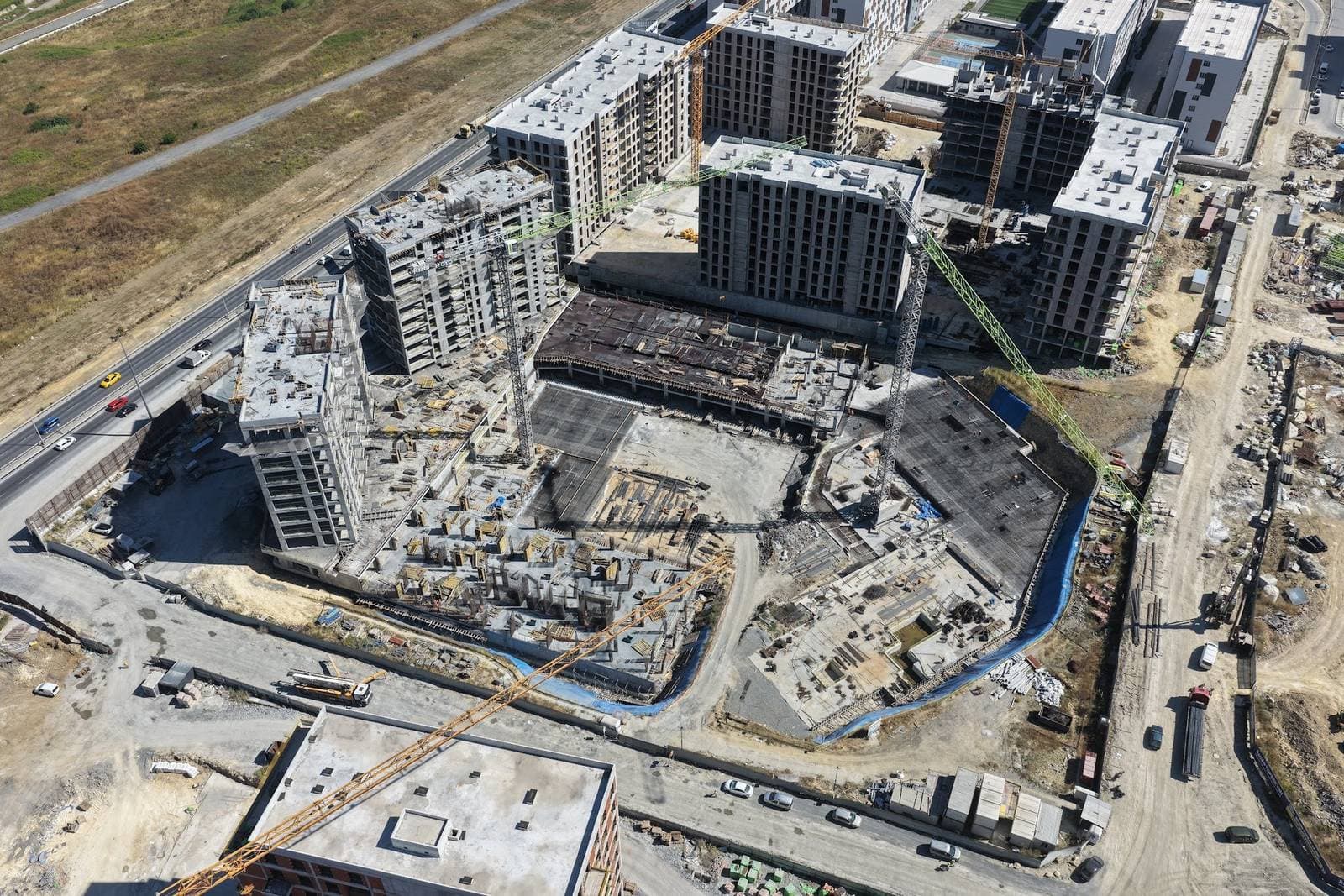 Drone photo of the construction site from above, with two concrete frames standing beside the boulevard and the basement and podium slabs of the other blocks under way