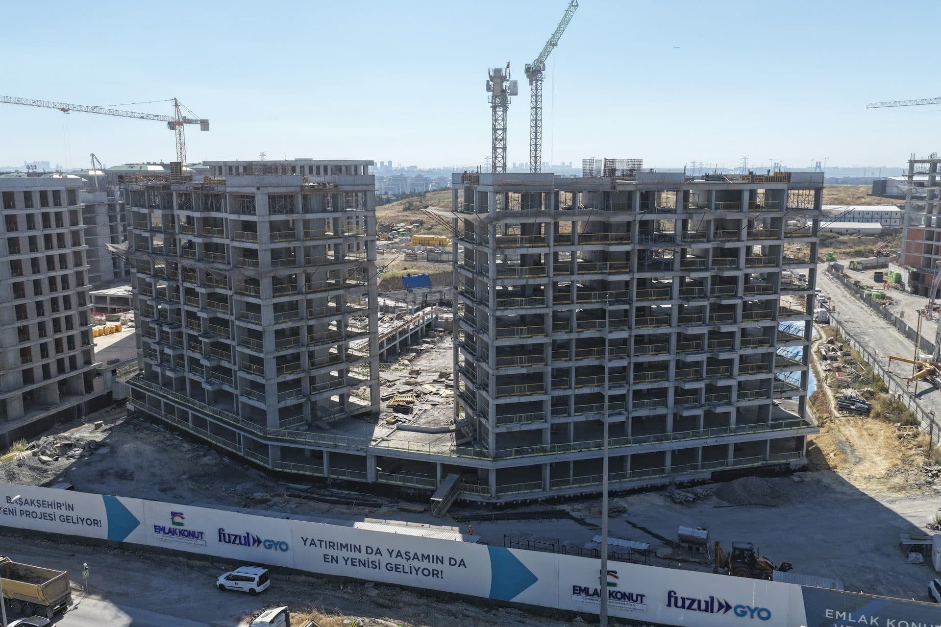 Drone photo of two topped-out concrete frames on a shared podium behind the developer's site hoarding
