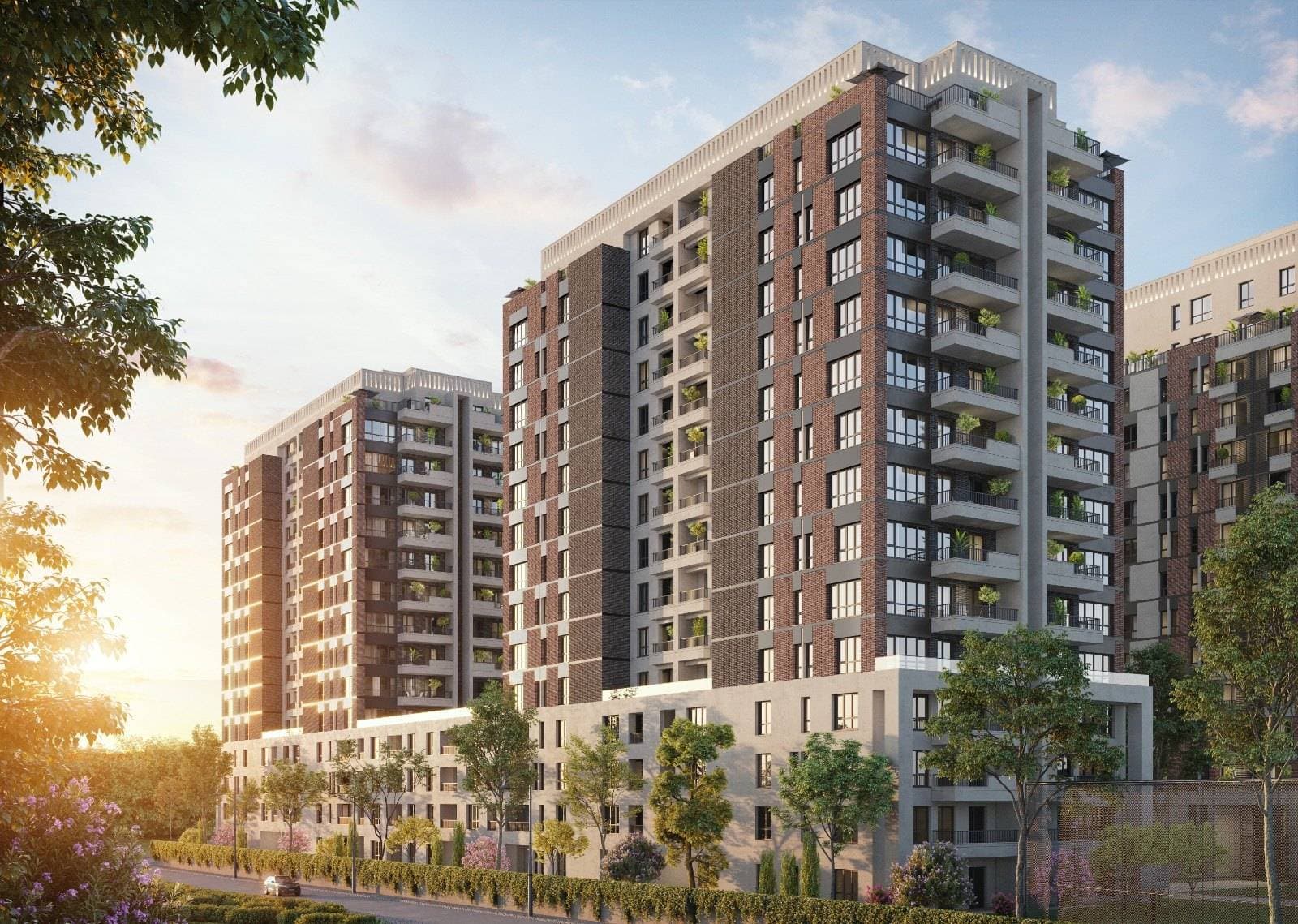Brown brick and light stone residential blocks of Avrupa Konutlari Esentepe at sunset, with trees and planting along the street in front