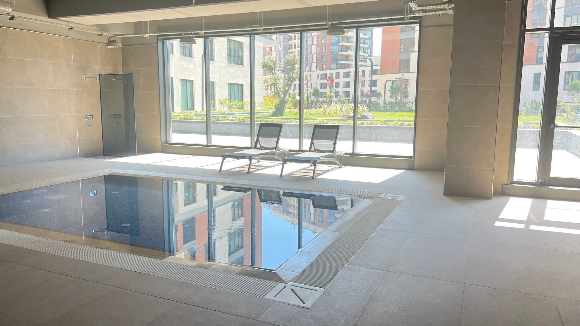 Indoor swimming pool with sun loungers and floor-to-ceiling windows looking onto the garden