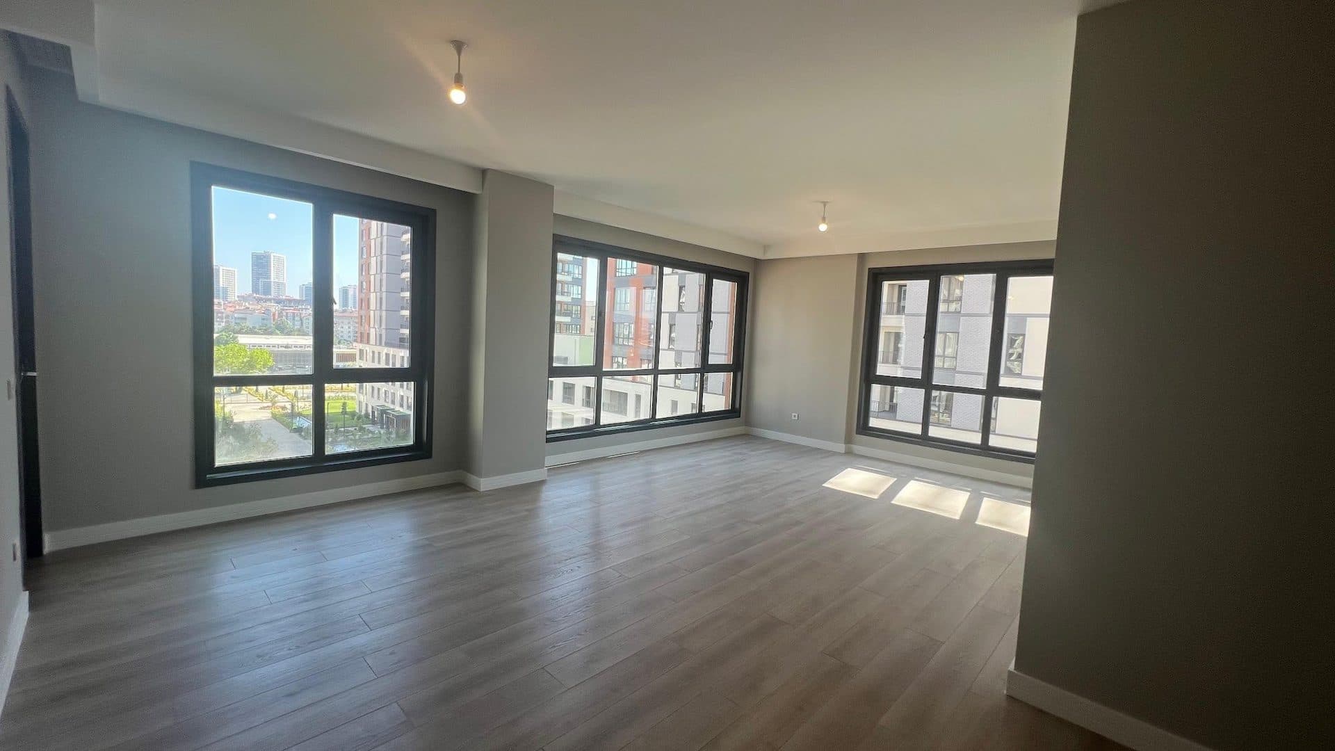 Empty living room of a finished sample apartment with wood-look flooring and three large windows