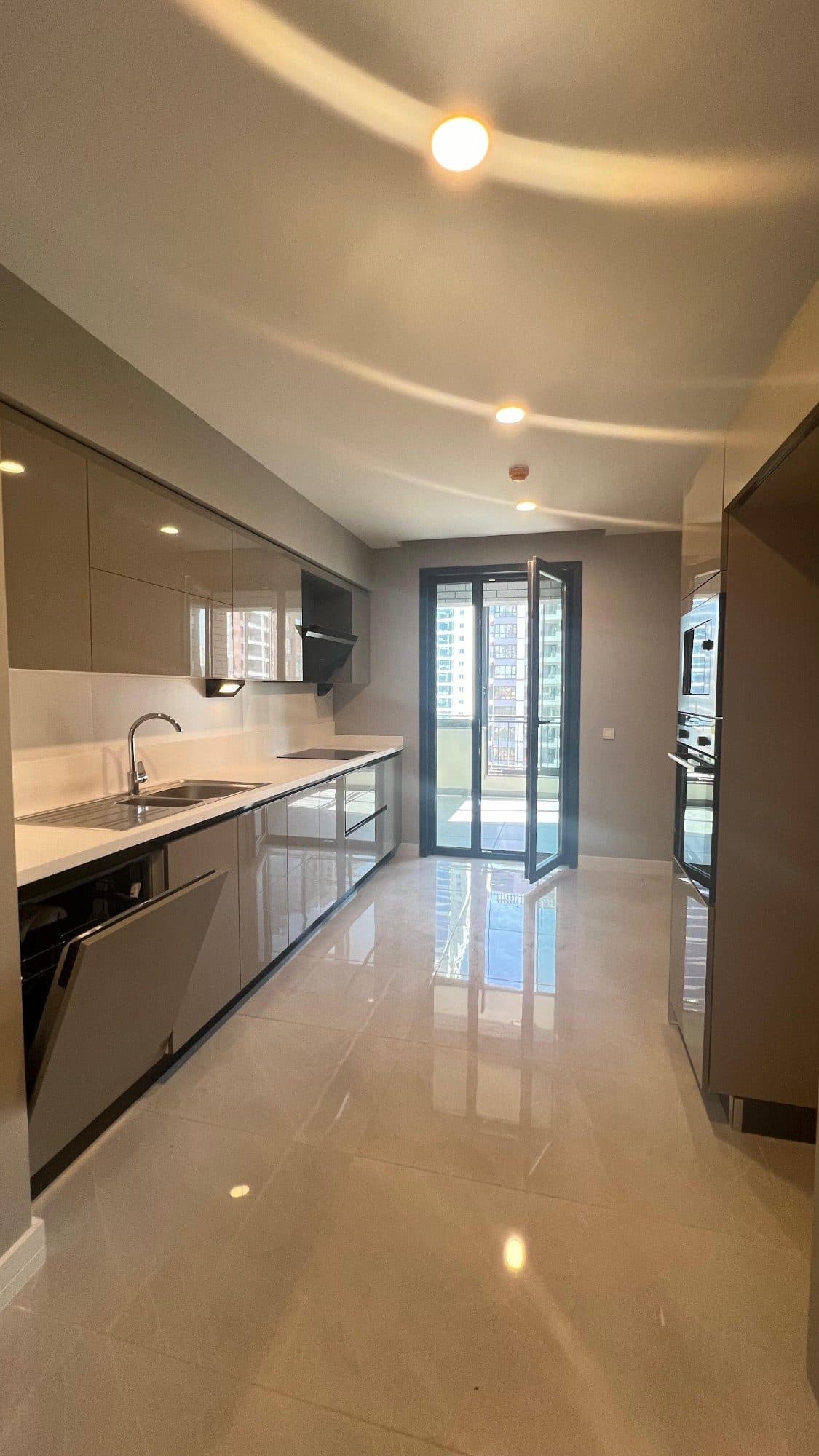 Fitted kitchen with gloss cabinets, a built-in oven, a dishwasher and a glazed door to the balcony
