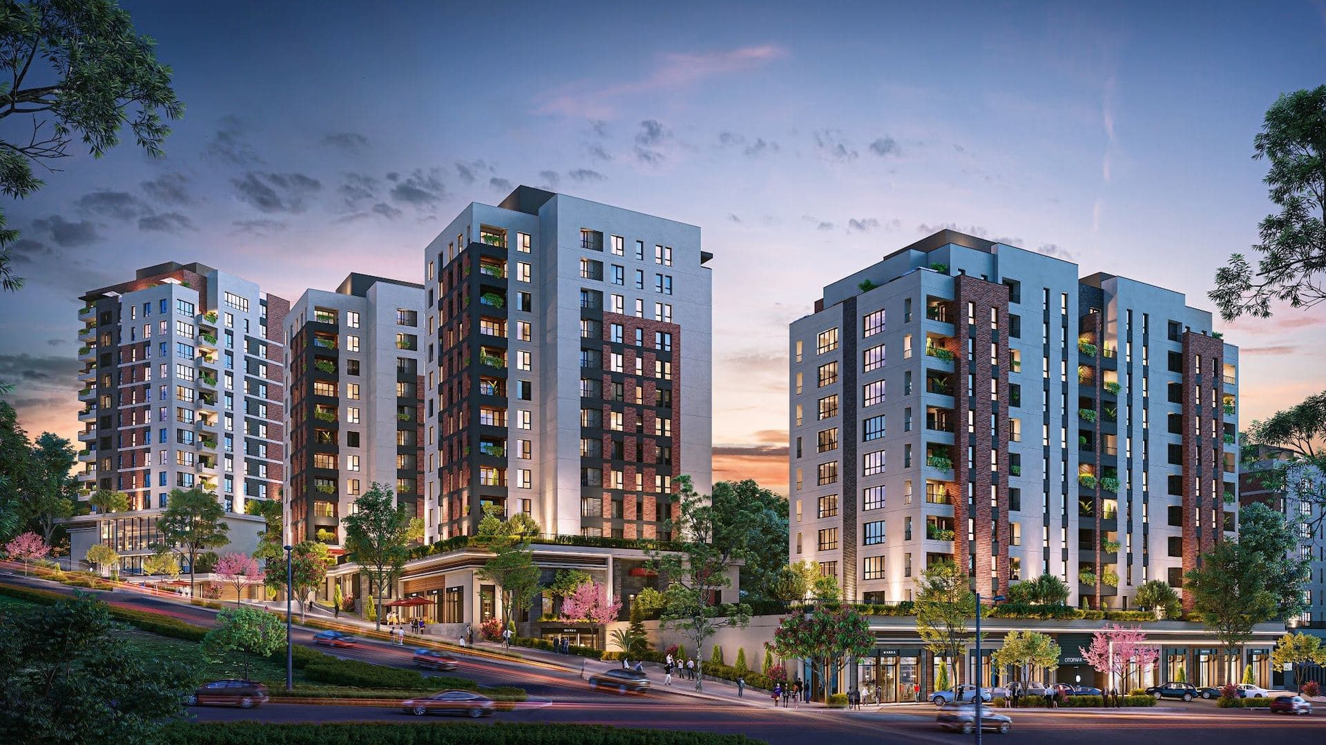 Residential blocks and shopfronts lit up at dusk beside the road