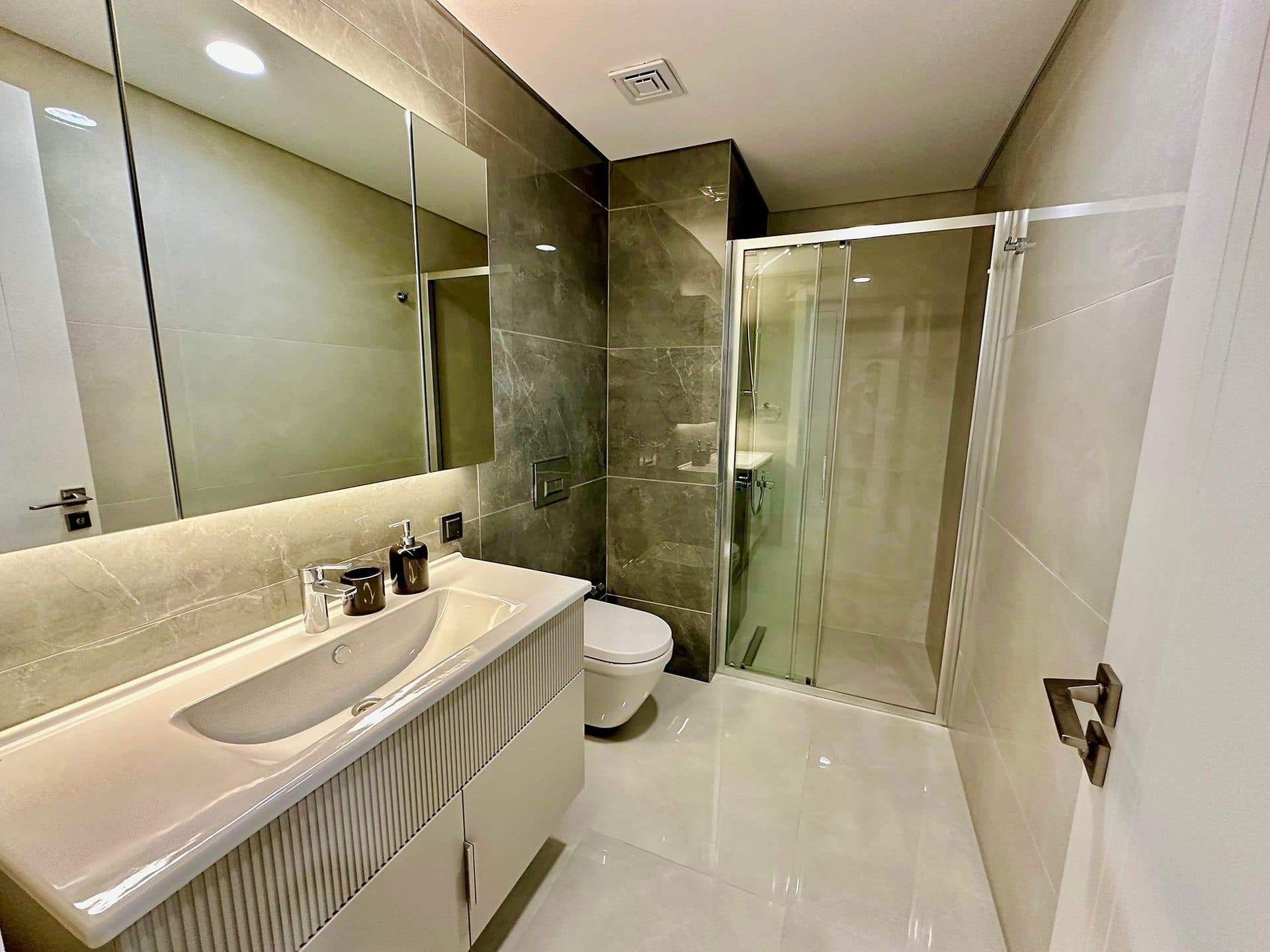 Bathroom of the 3+1 sample apartment with a glass shower, wall-hung toilet and long vanity unit