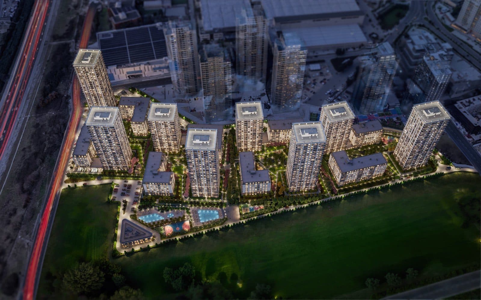 Night aerial view of the whole complex beside the motorway, with lit towers, landscaped courtyards and two pools