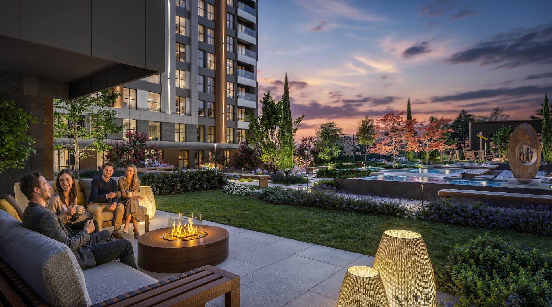 Evening seating around a fire table on a courtyard terrace, with lawns, pools and a lit block behind