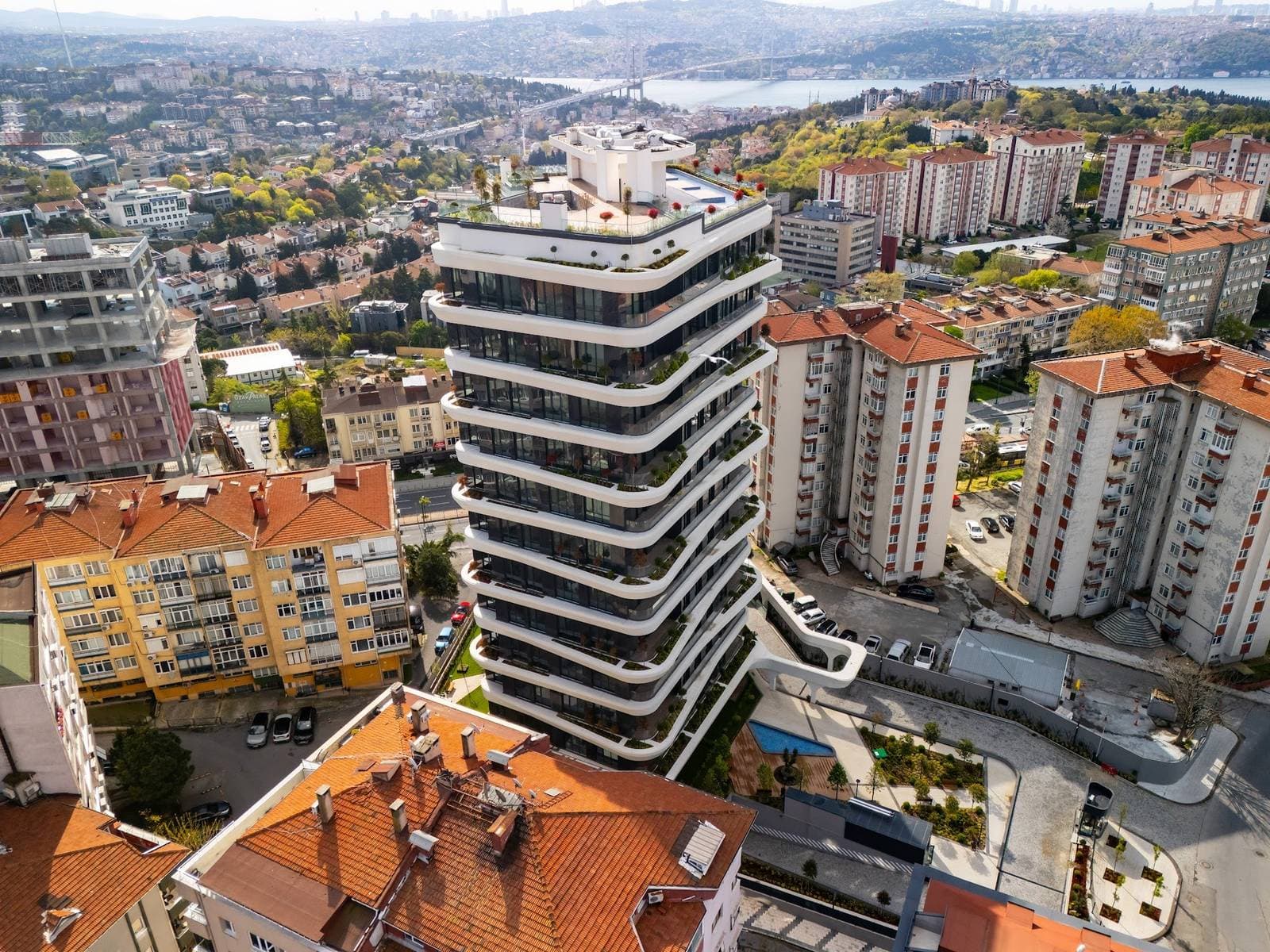 Drone photo of the tower from above, with its roof terrace, planted balconies and garden pool, and the Bosphorus Bridge and the Asian shore beyond