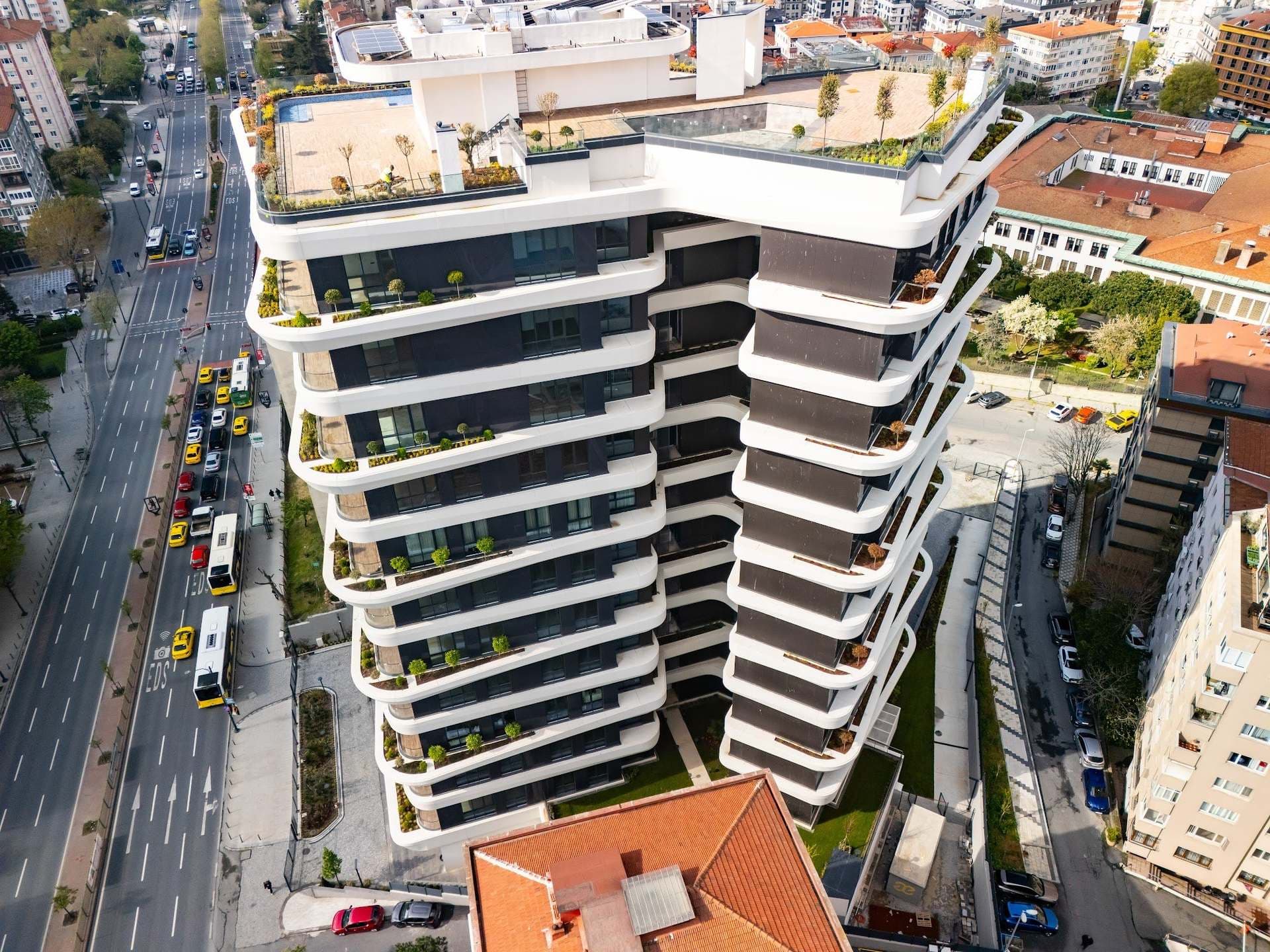 High drone view of the tower's two wings with planted terraces and the roof terrace, beside the lanes of Barbaros Boulevard
