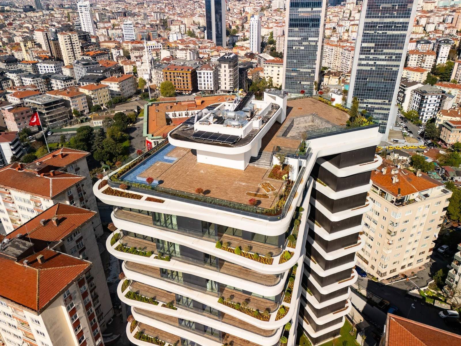 Drone photo of the roof terrace with a wooden deck, a tiled pool basin and planted edges above the curved, planted balconies