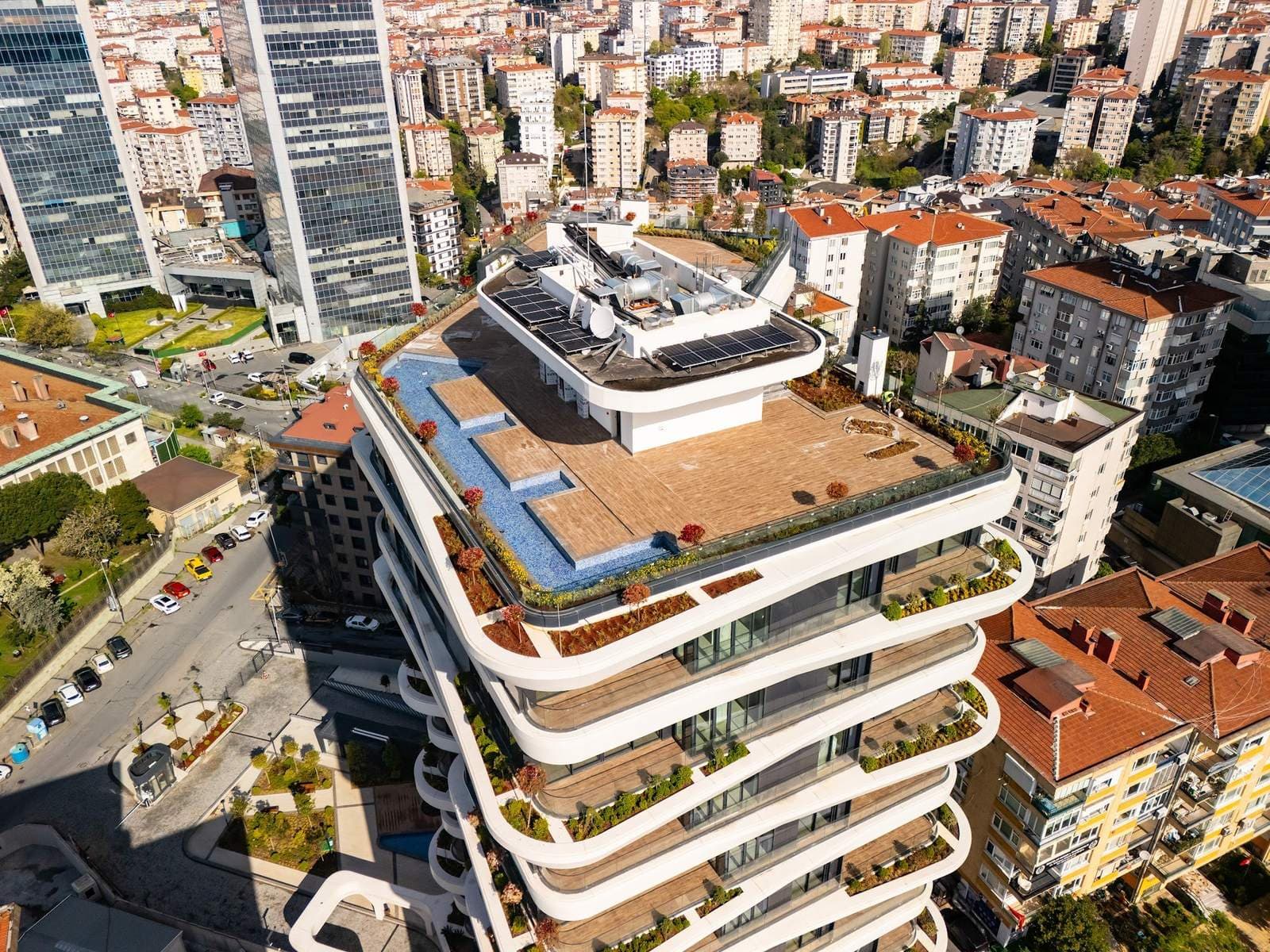 Drone view down onto the roof terrace and the stacked curved terraces, with the landscaped entrance garden and its pool below