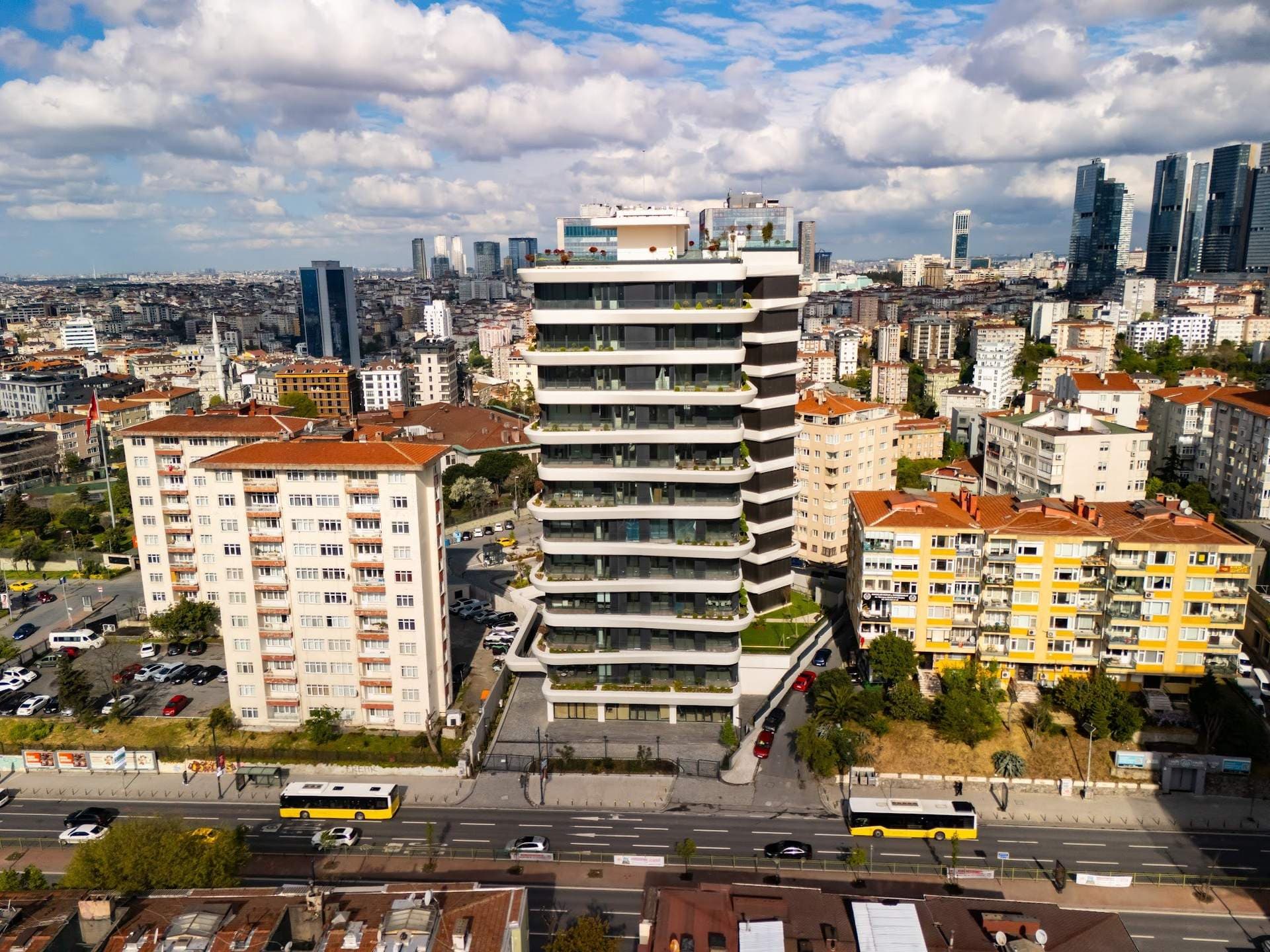 Drone photo of the finished tower on Barbaros Boulevard between older apartment blocks, with city buses passing in front