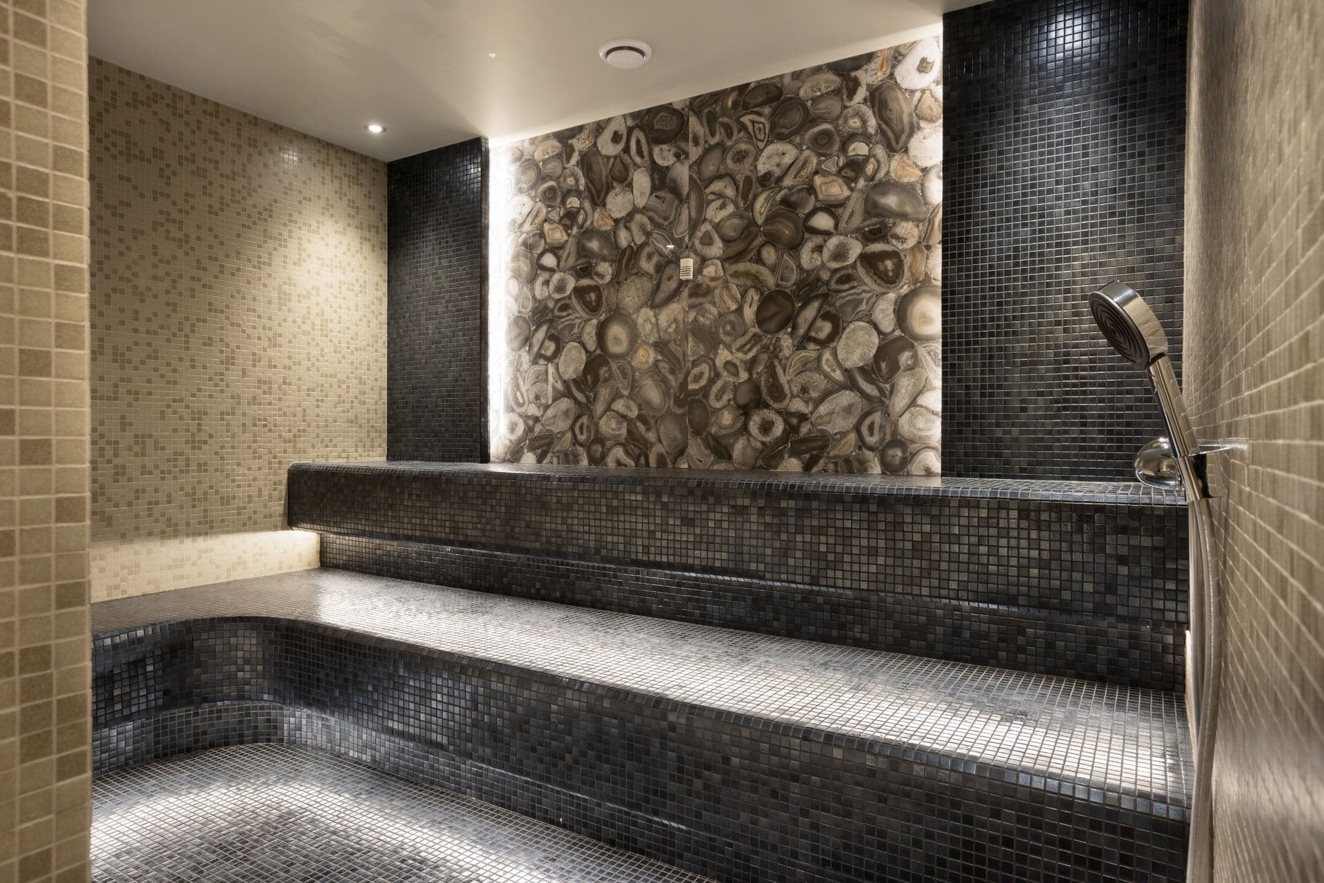 Steam room with mosaic-tiled benches and a stone feature wall