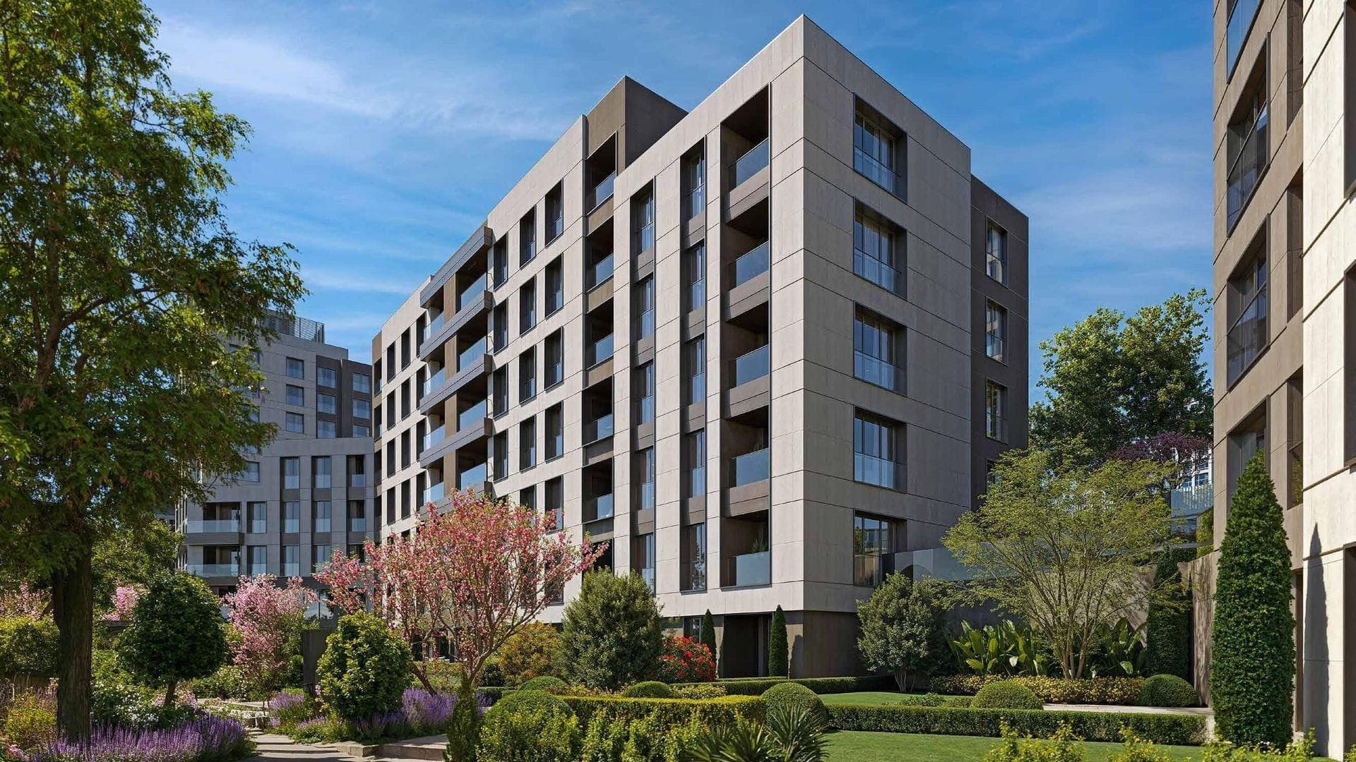 A residential block with balconies above landscaped gardens and flowering trees on a sunny day