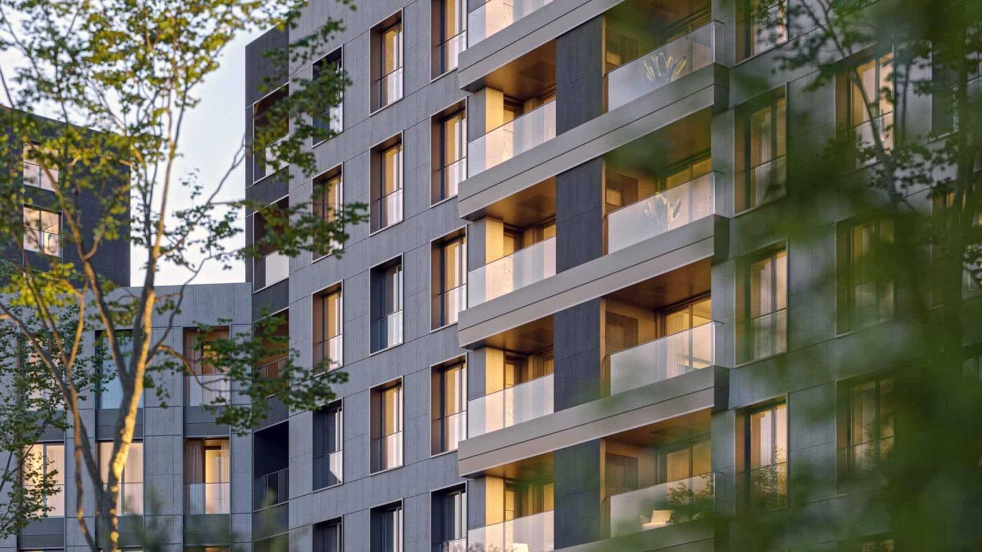Close view of the facade with deep balconies and glass railings, framed by trees