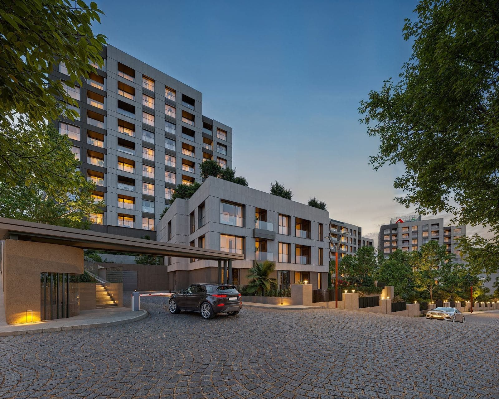 Gated vehicle entrance with a barrier and a canopy below the residential blocks at dusk