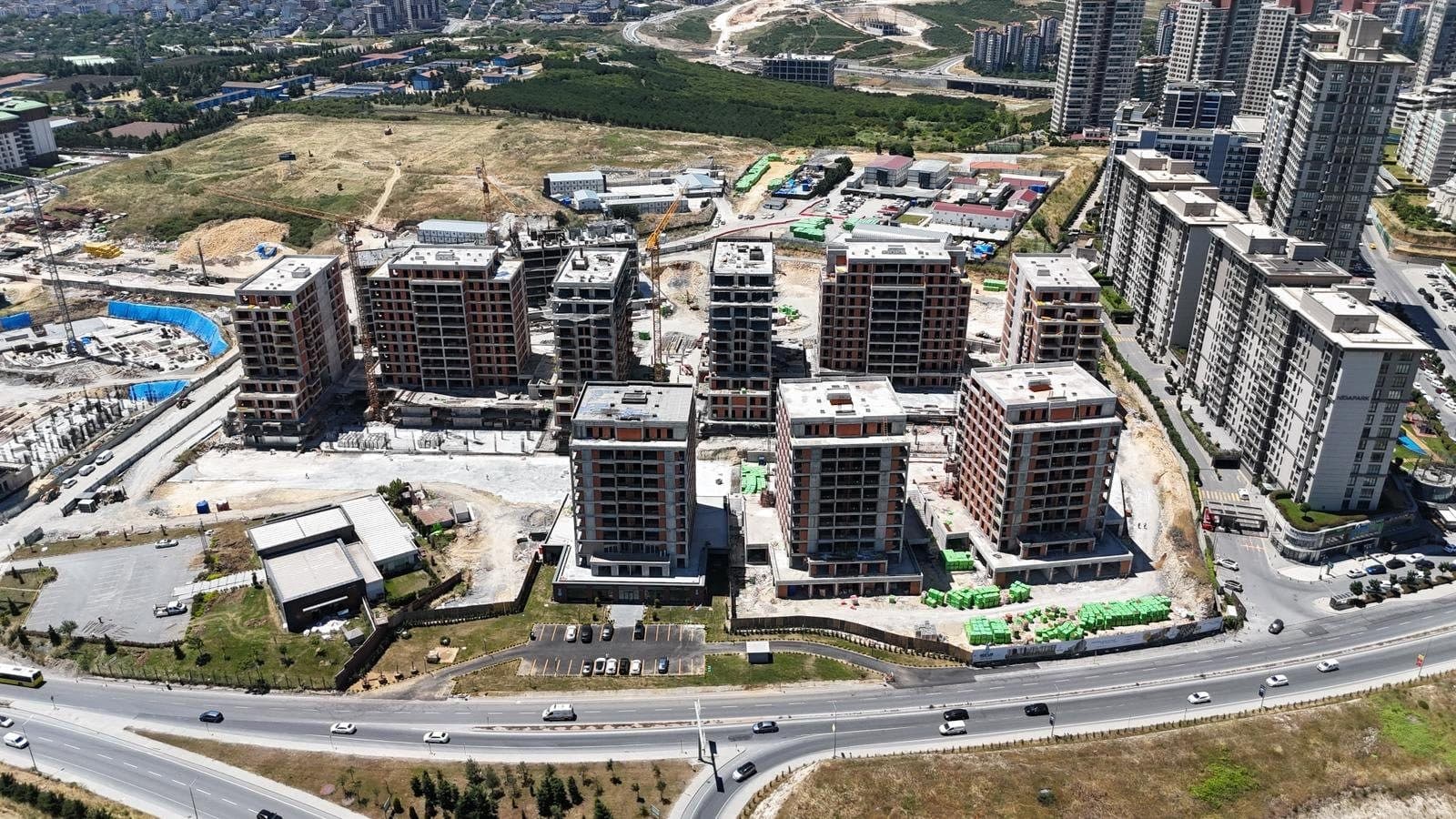 Drone photo from June 2026 of the blocks under construction seen across the boulevard, most at full height with brick infill on the upper floors