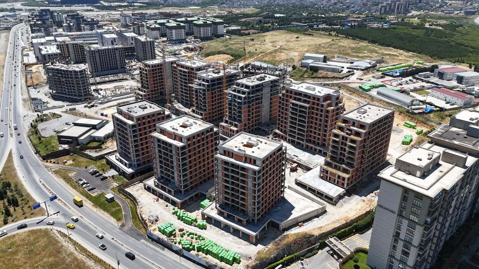 Drone photo from June 2026 looking along the site, with the blocks in brick and concrete shell and the boulevard on the left