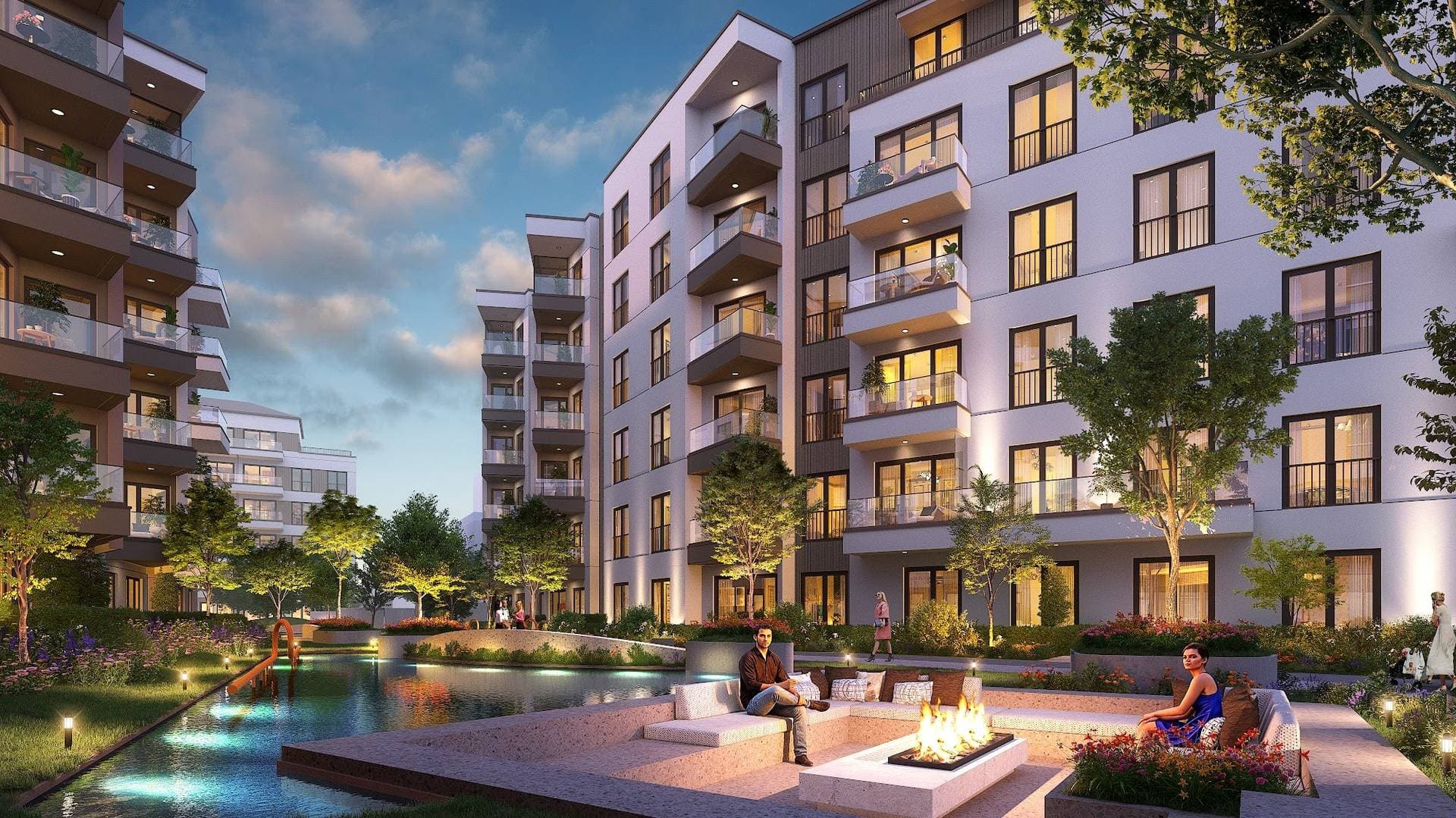 Evening view of the courtyard with a lit water channel, fire pit seating and residential blocks behind