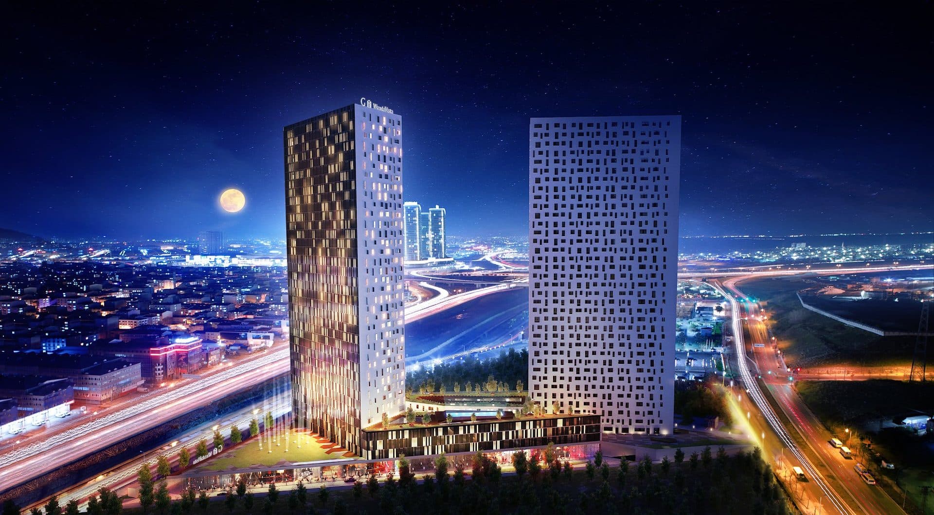 Night render of the whole complex: the Wanda Vista hotel tower and the white G Yoo tower on a shared landscaped podium beside a busy motorway interchange, with the city lights behind