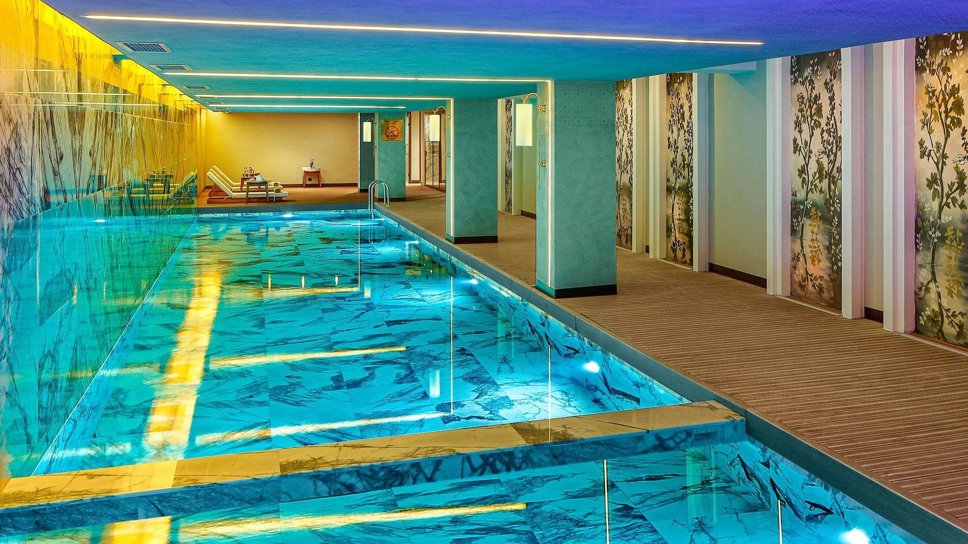 Heated indoor swimming pool with turquoise mosaic tiles, square columns and a timber deck along one side