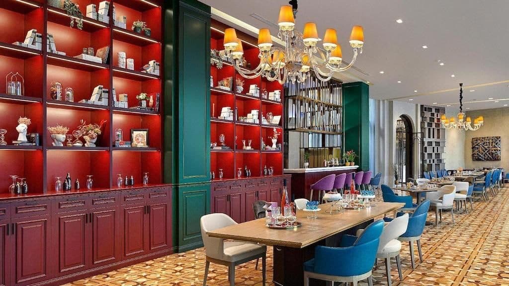 Bistro and lounge with red-lit display shelving, a crystal chandelier, a long communal table and blue dining chairs