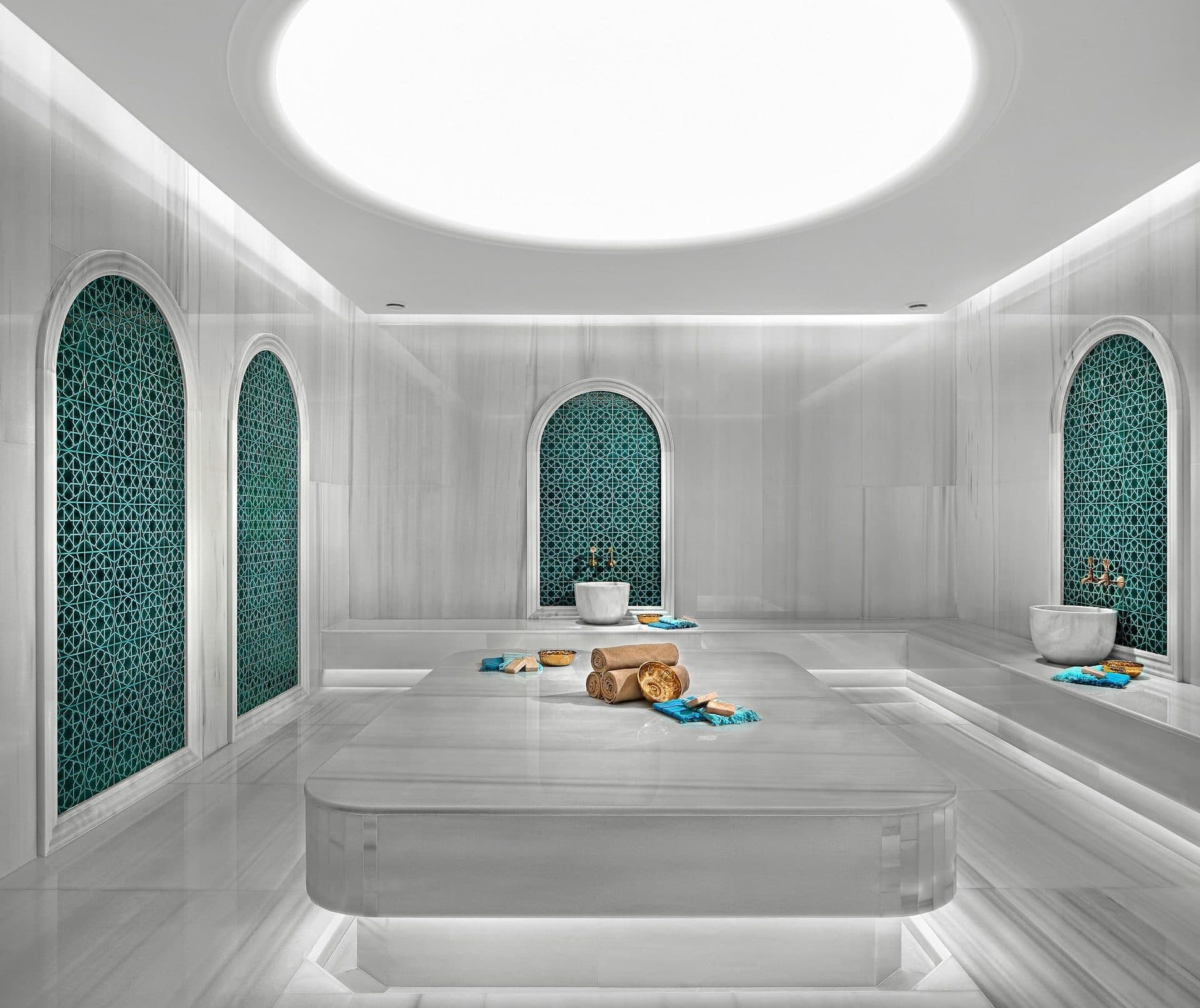 Turkish bath in white marble with a central heated platform, arched niches with green lattice tiles and a round skylight