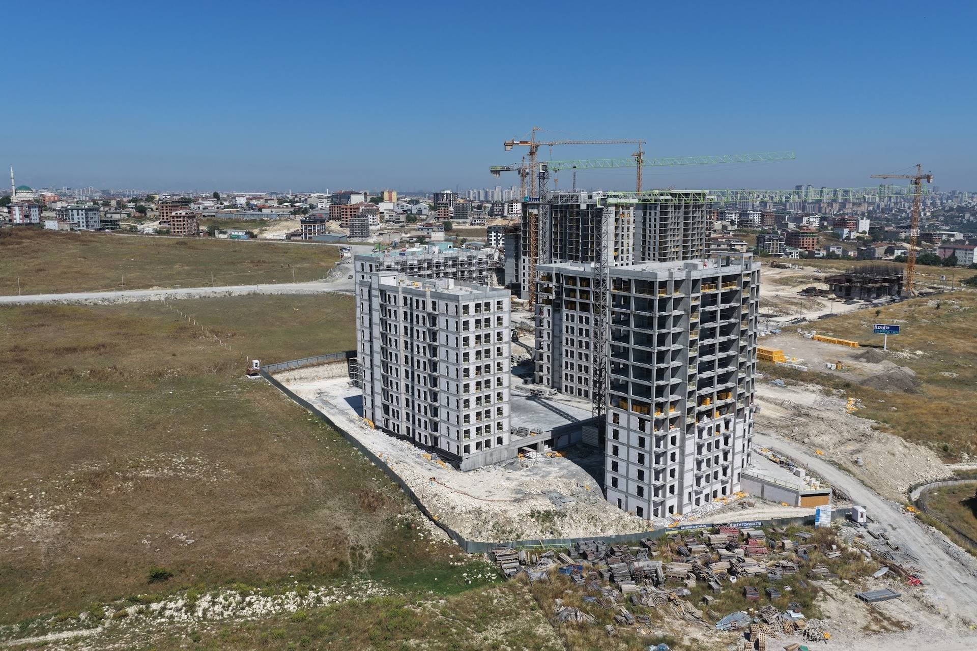 Drone photo of the four blocks under construction on an open site, with tower cranes and housing in the background