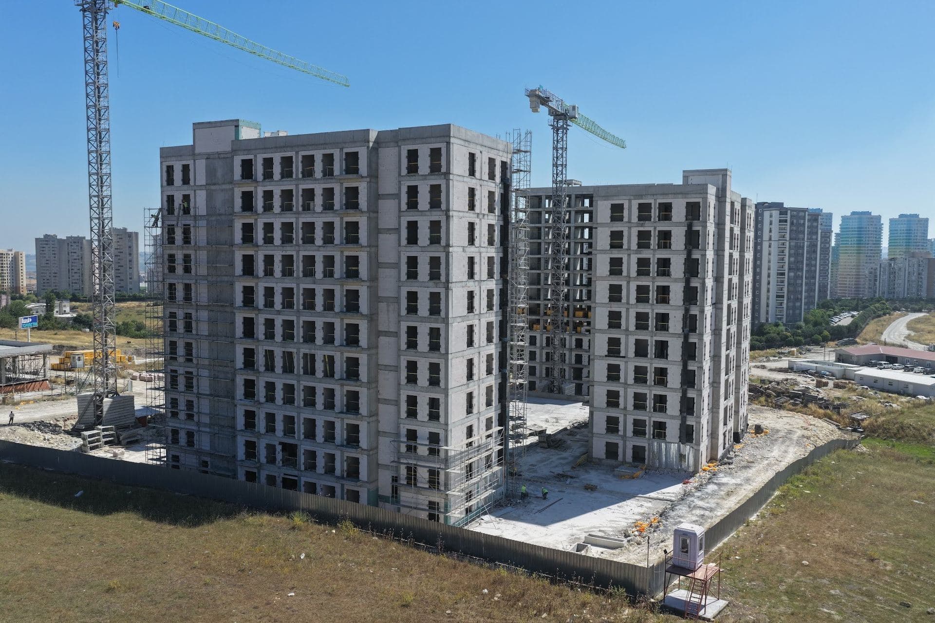 Drone photo of two blocks under construction with scaffolding and tower cranes inside the fenced site