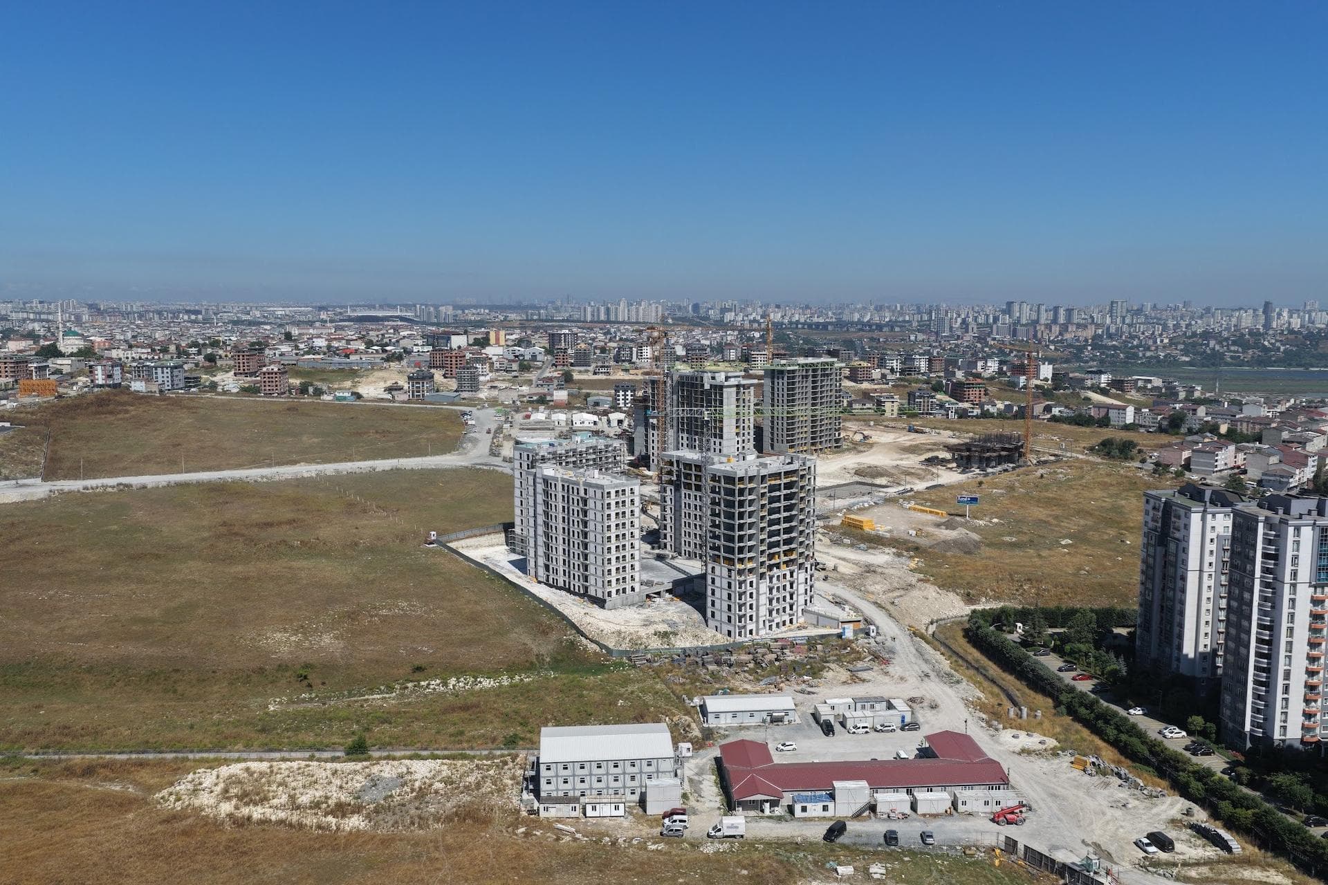 Wide drone photo of the construction site with its four blocks, site offices in front and the city skyline behind
