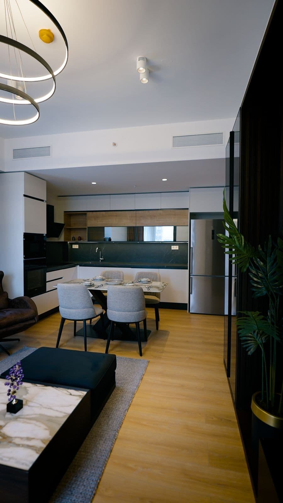 Open-plan living area of the sample apartment, with a dining table and the fitted kitchen beyond