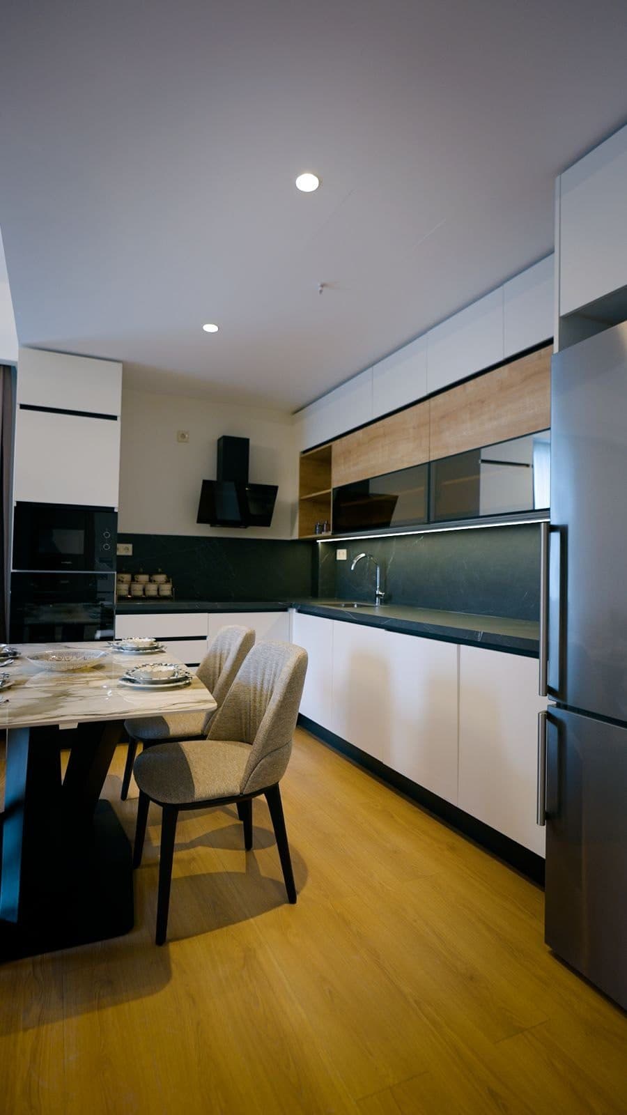 Fitted kitchen of the sample apartment with white and wood-tone cabinets, a built-in oven and a dining table