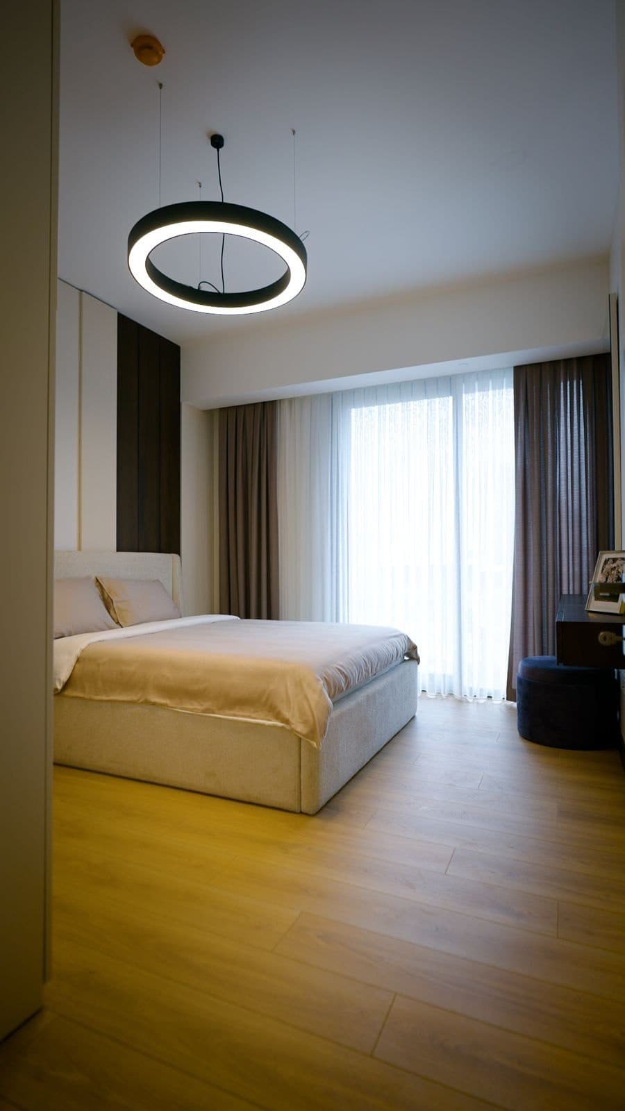 Bedroom of the sample apartment with a double bed, wood-look floor and a full-height window with curtains
