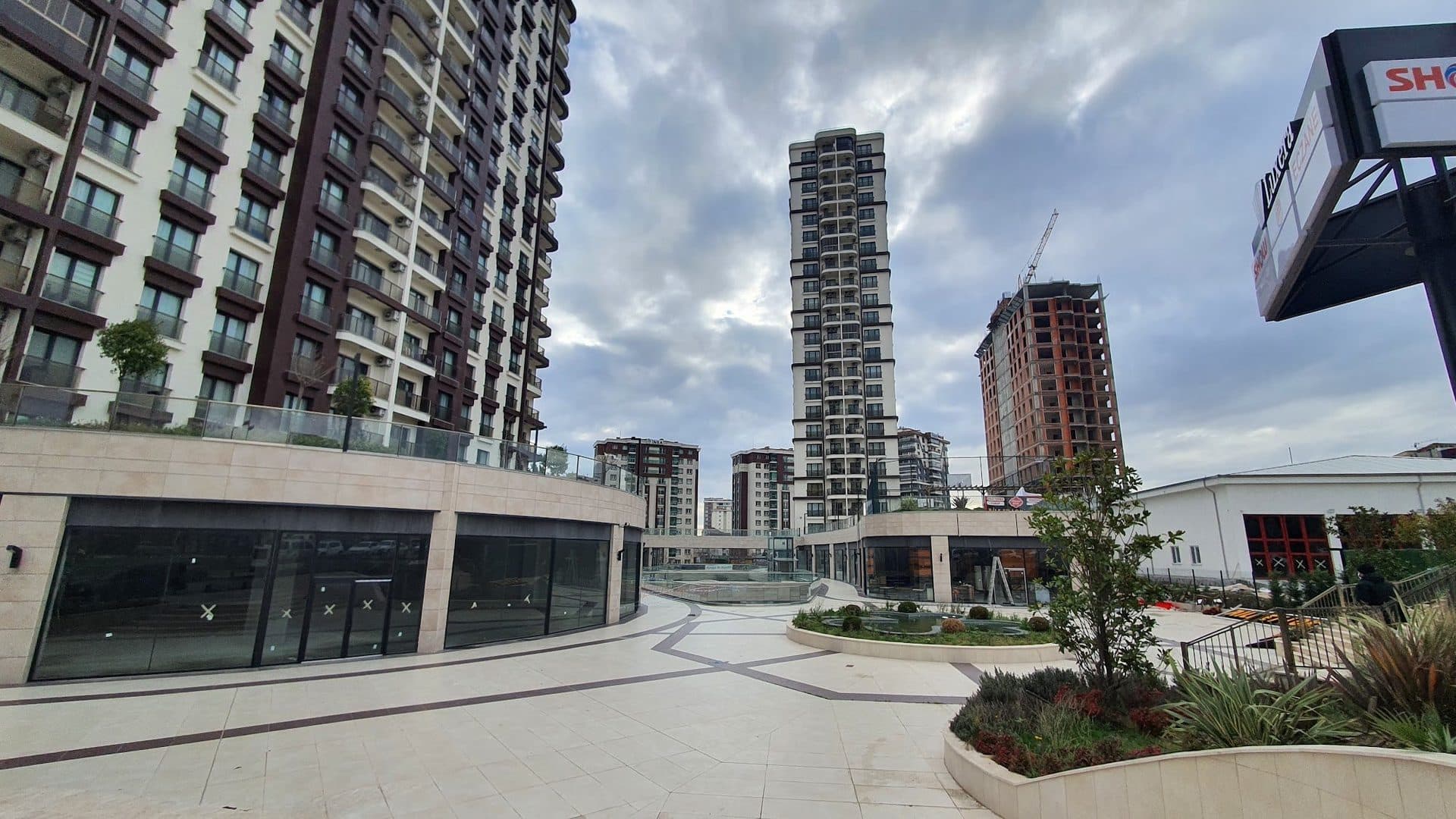 Upper level of the shopping street with planters and a fountain, a residential tower on the left
