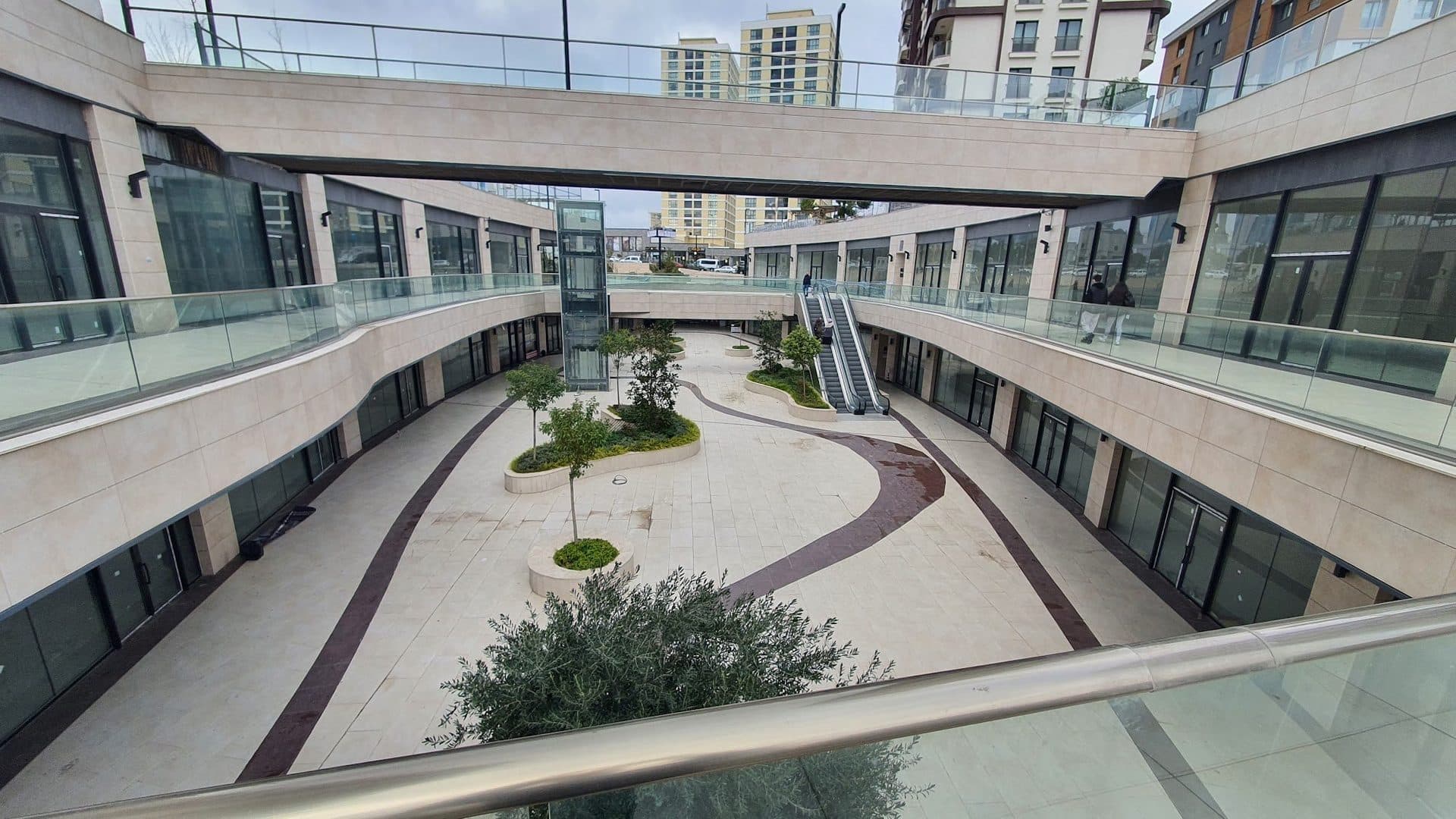 Lower shopping street seen from the upper walkway, with planted islands and escalators