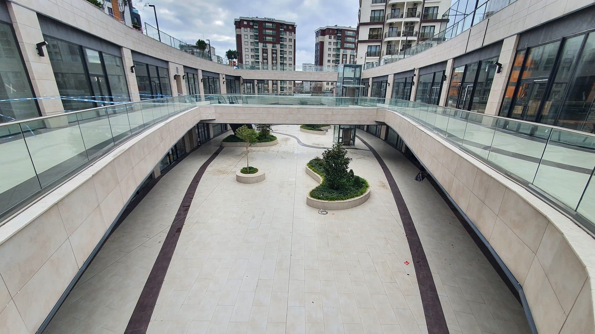 Lower shopping street between two levels of glazed shopfronts, seen from a footbridge