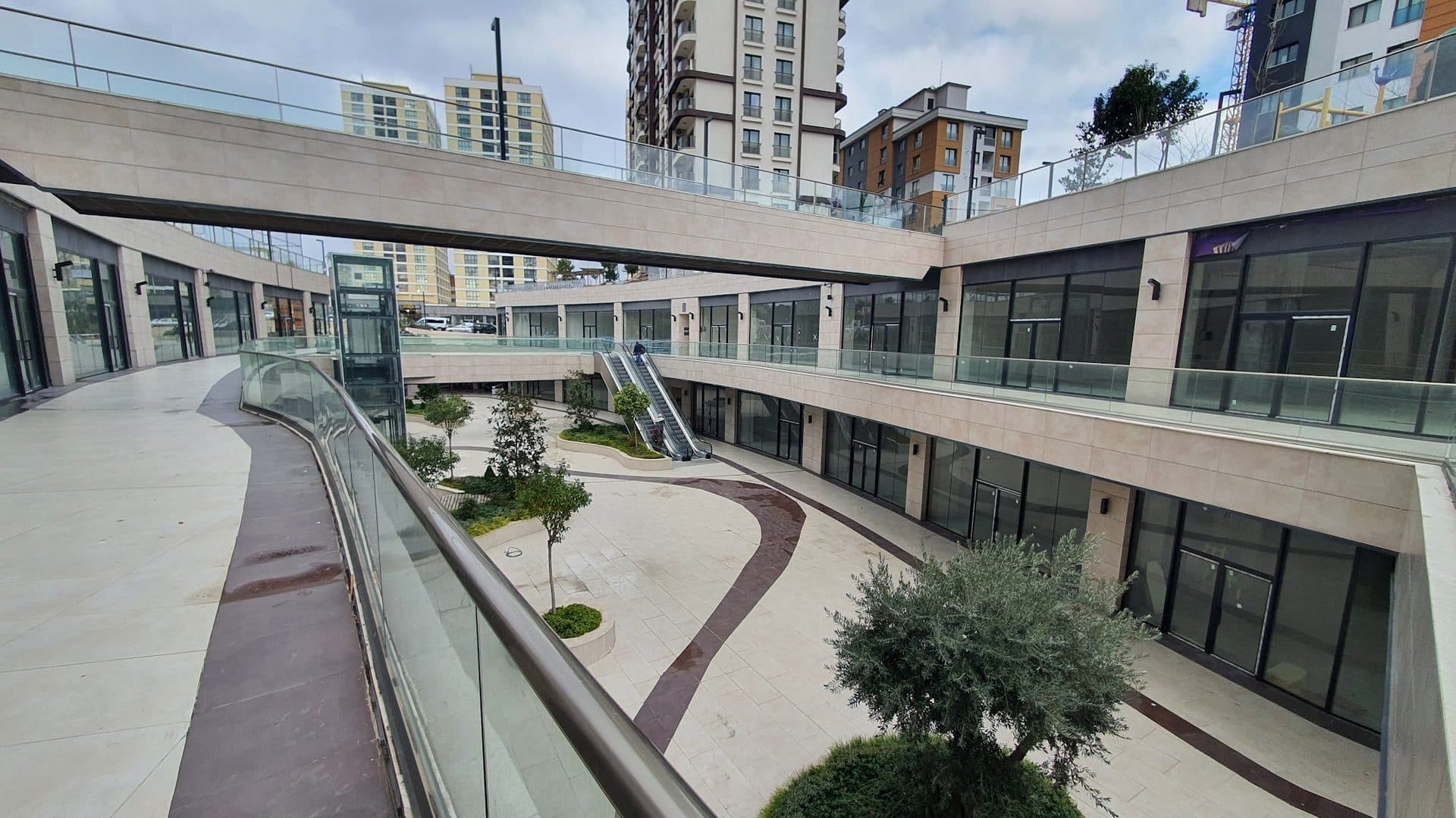Curved upper walkway with a glass balustrade overlooking the landscaped lower street