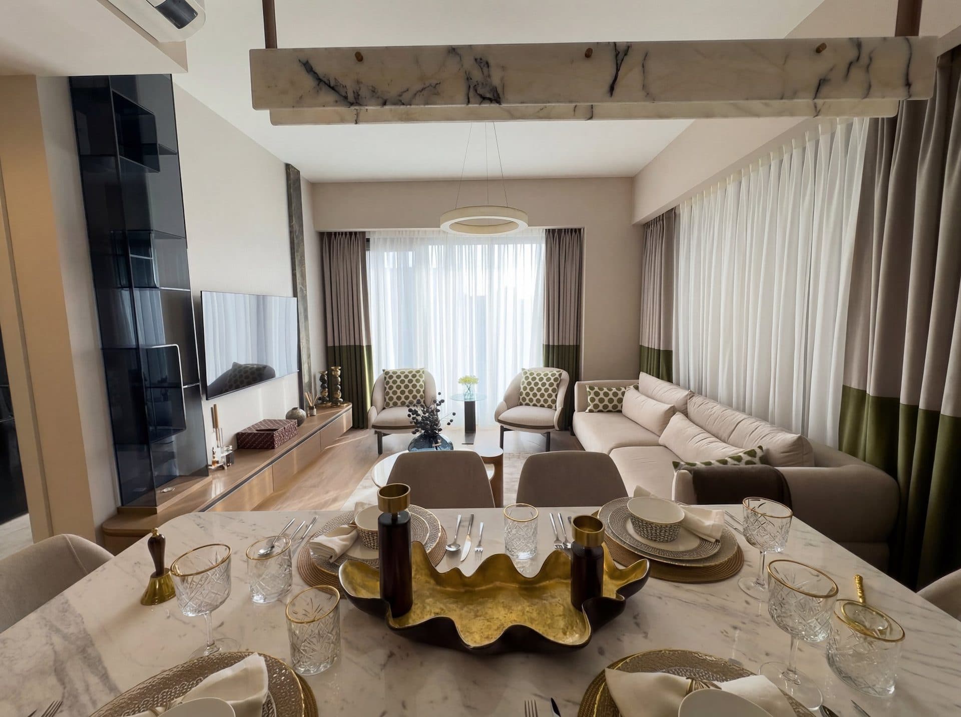 Photo of the furnished 2+1 show apartment: living and dining room with a marble dining table, a corner sofa and floor-length curtains