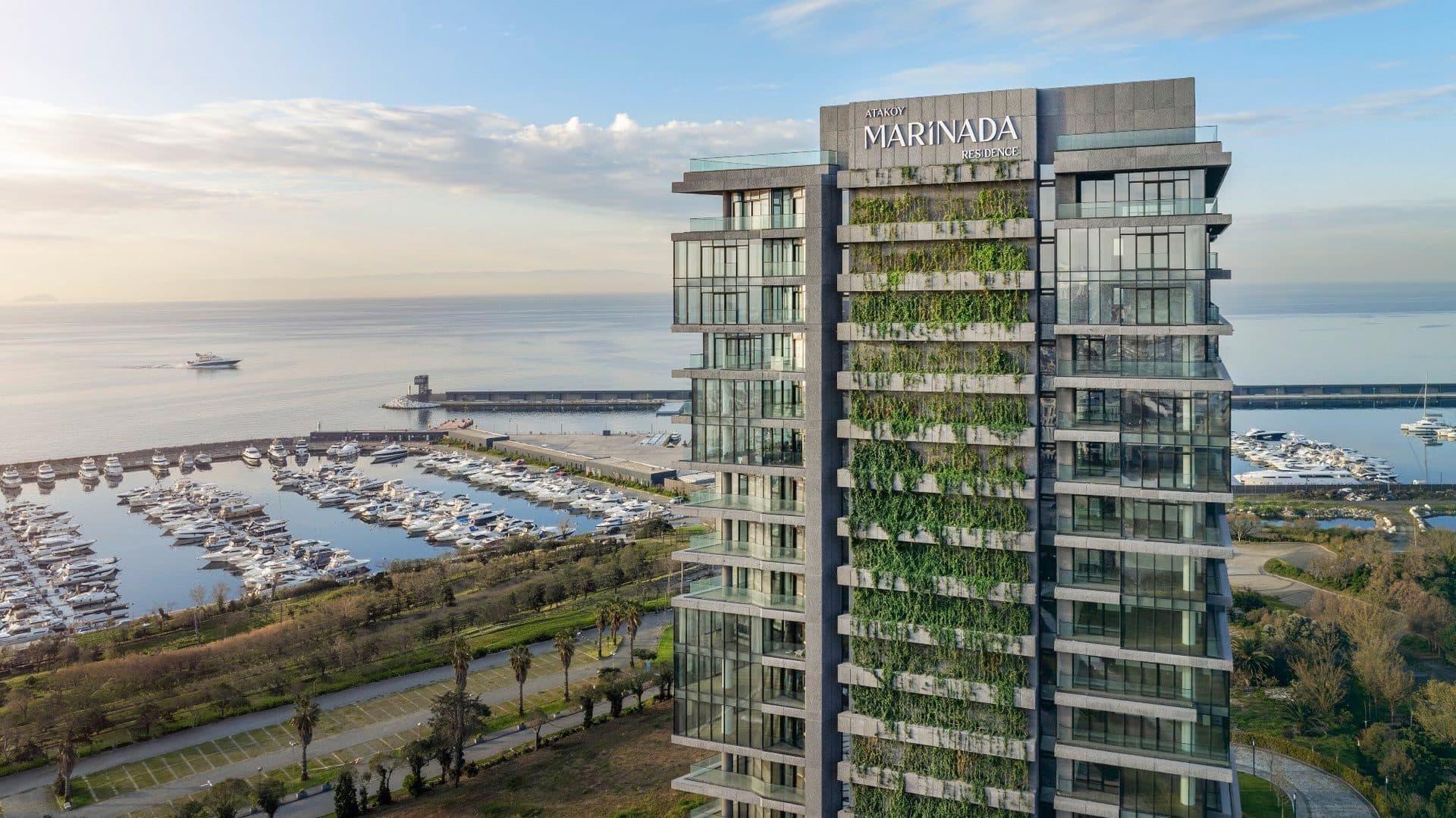 Close aerial view of the tower's glass facade and vertical garden, with the yacht basin and breakwater behind