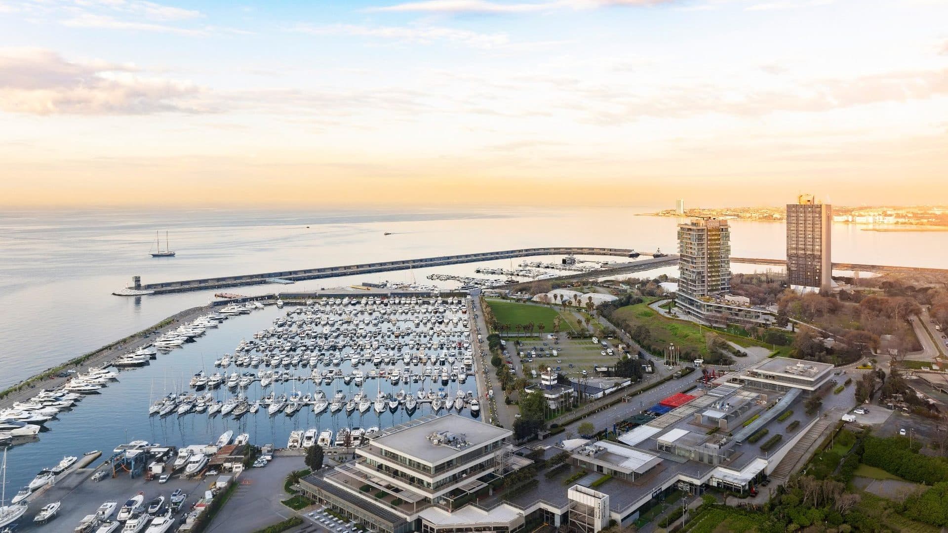Aerial view over Atakoy Marina's yacht basin and breakwater, with the tower and a neighboring hotel tower on the right