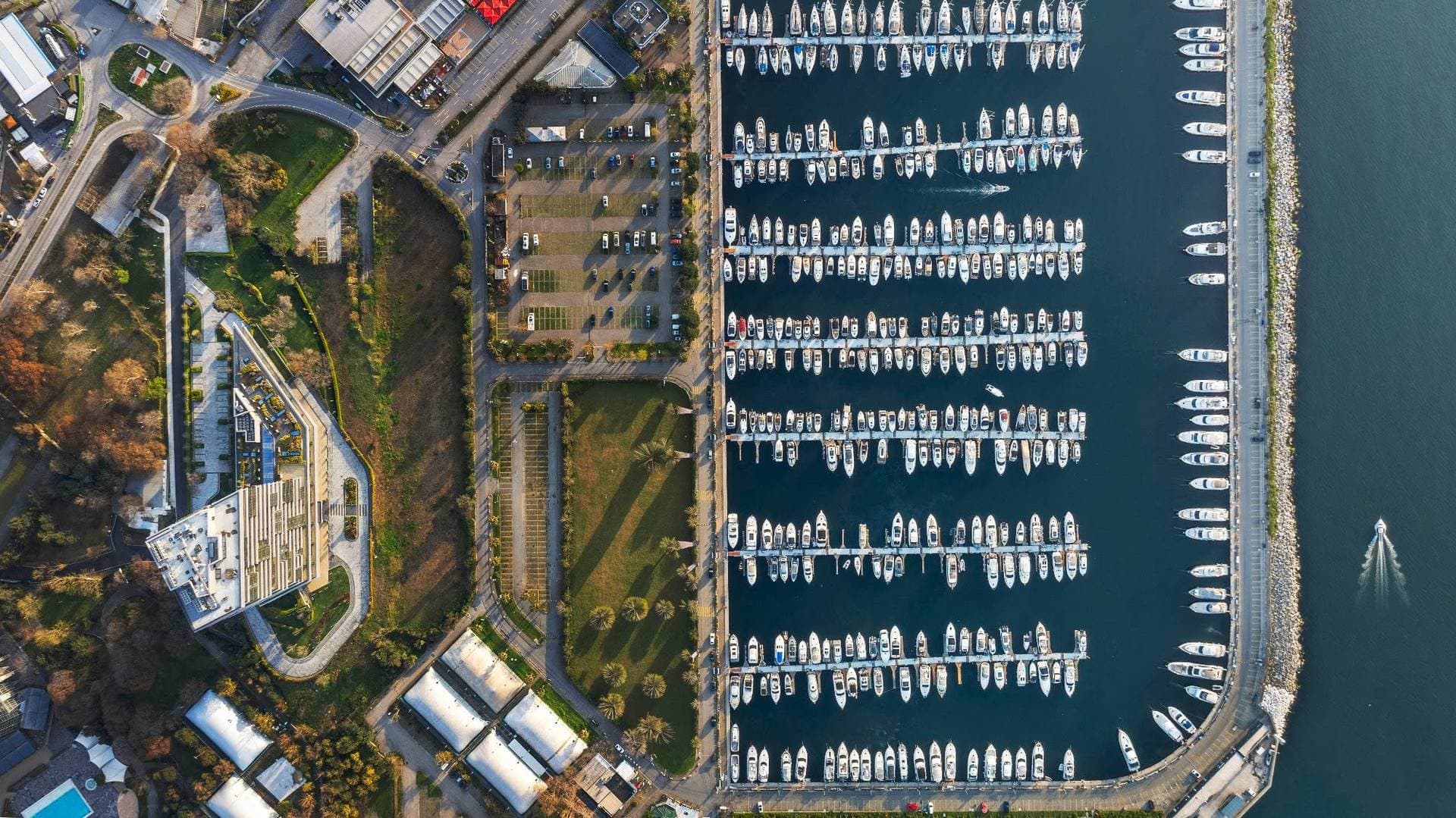 Top-down drone view of the tower's roof and gardens next to the marina's parking area and yacht berths