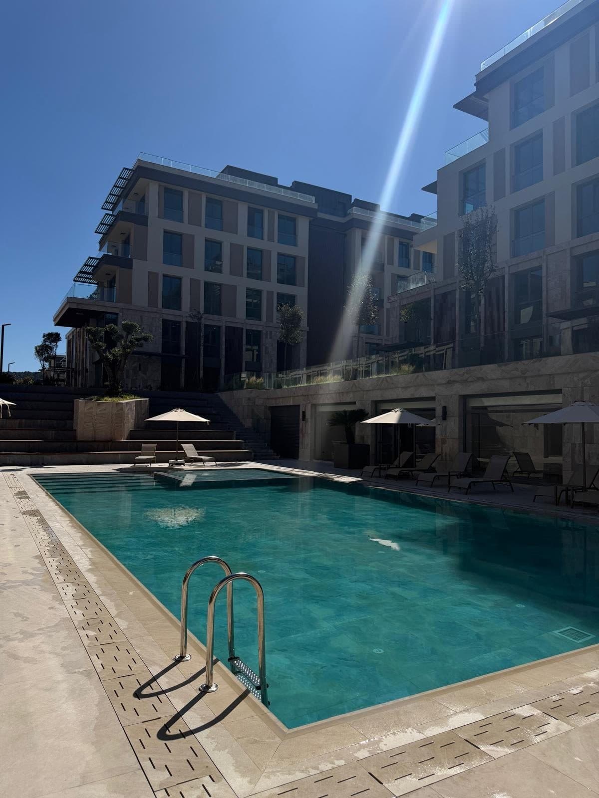 Photo of the outdoor pool with a steel ladder and the facades of two finished blocks under a clear sky