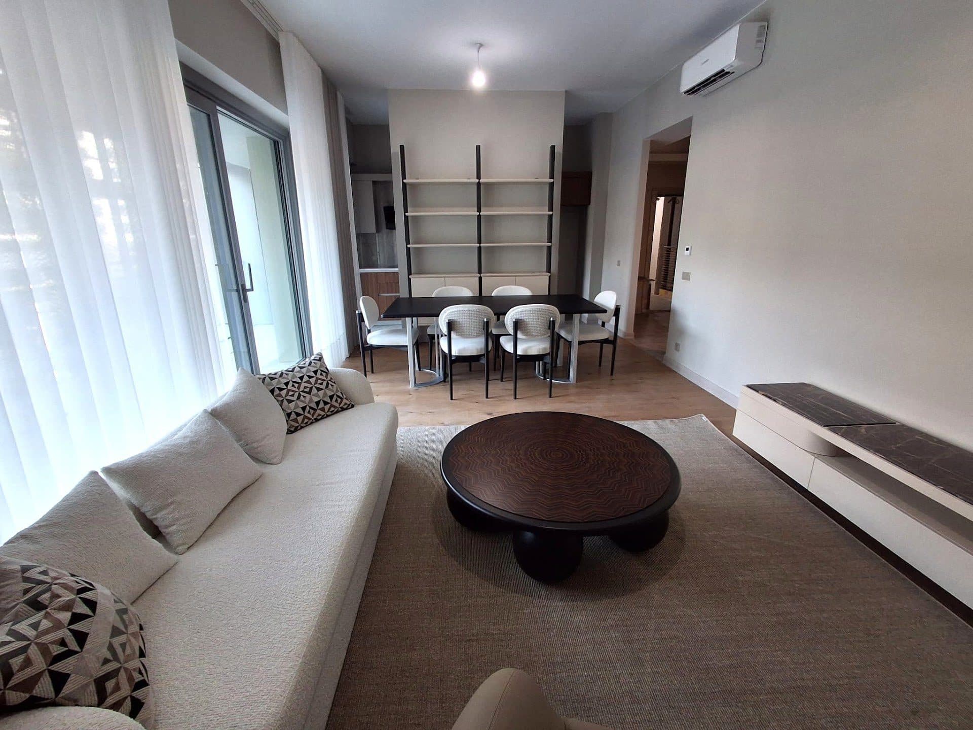 Living and dining room of the show apartment, with a sofa, a round coffee table and a dining table by the window