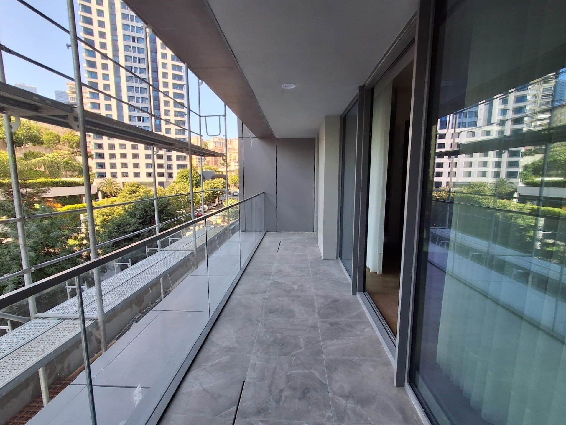 Long balcony with a glass balustrade outside the floor-to-ceiling windows, with neighboring high-rises in view